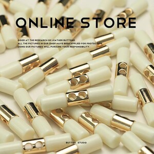 Pode incluir: Um close-up de um grupo de botões de alternância de plástico branco com detalhes em metal dourado. Os botões estão dispostos em um padrão aleatório. O texto "ONLINE STORE" e "BUTTON STUDIO" é visível na imagem.