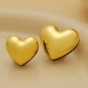 Puede incluir: Dos pendientes de oro en forma de corazón. Los pendientes son brillantes y tienen una superficie lisa.