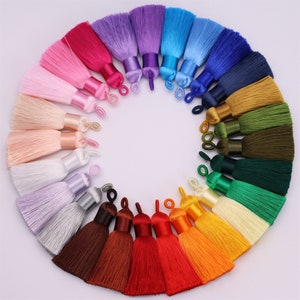 Puede incluir: Una colección de 20 borlas de seda de colores, cada una de un color diferente, dispuestas en círculo. Las borlas están hechas de un material suave y sedoso y tienen una franja delicada. Son perfectas para añadir un toque de elegancia a cualquier proyecto.