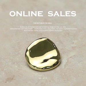 Könnte beinhalten: Ein goldfarbener Knopf mit unregelmäßiger, organischer Form. Der Knopf ist glatt und reflektierend, mit dem Text "ONLINE SALES" oben und "THE BUTTON IS THE SOUL" darunter. Der Text "JUST MET U" befindet sich unten.