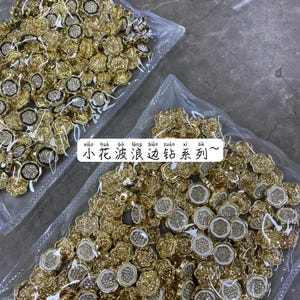 Könnte beinhalten: Nahaufnahme einer großen Menge goldfarbener, blumenförmiger Knöpfe mit weißen Strasssteinen in der Mitte. Die Knöpfe sind in durchsichtigen Plastiktüten verpackt. Der Text "xiao hua bo liang bian zuan xi lie ~" ist im Bild sichtbar.