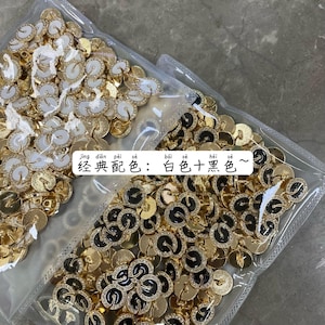 Könnte beinhalten: Zwei Beutel mit goldfarbenen Metallknöpfen mit weißem und schwarzem Email. Der Text auf dem Beutel lautet "Jing dian pei se: Bai se + Hei se ~".