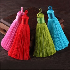 May include: Five colorful tassel ornaments with a long, thin fringe. The tassels are pink, red, green, and blue.