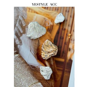 May include: Four abstract, textured metal brooches in silver and gold tones. The brooches have an organic, wave-like design. The top of the image has the text "YESTYLE ACC".