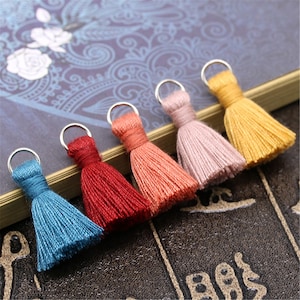 Pode incluir: Cinco borlas coloridas com argolas prateadas. As borlas são em tons de azul, vermelho, laranja, rosa e amarelo.
