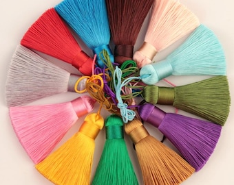May include: Assortment of 12 colourful silk tassels in various shades, including red, blue, green, purple, pink, brown, and grey. The tassels are arranged in a circle, with the tips of the tassels pointing outwards.