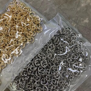 Könnte beinhalten: Zwei Beutel mit Metallkettengliedern, ein Beutel enthält goldfarbene Glieder und der andere silberfarbene Glieder.