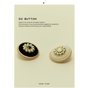 May include: Two decorative buttons, one black with a gold center and one white with a gold center. Both buttons have a gold beaded border.