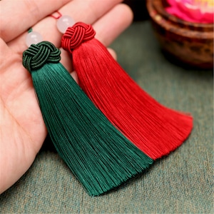 May include: Two tassel ornaments with a knotted top and a white bead. The tassel on the left is green and the tassel on the right is red.