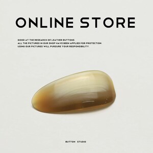 May include: A polished, oval-shaped button with a gradient of colors, transitioning from a light cream to a warm brown. The text "ONLINE STORE" is at the top, with additional text below. The words "BUTTON STUDIO" are at the bottom.