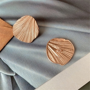 Może przedstawiać: Dwa guziki w kształcie muszli w kolorze różowego złota. Guziki mają teksturowaną, prążkowaną powierzchnię. Jeden guzik jest skierowany w górę, a drugi w dół, odsłaniając tył z tekstem "20011" i "104".