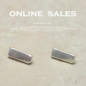 Könnte beinhalten: Zwei rechteckige, irisierende Knöpfe mit abgerundeten Kanten. Die Knöpfe sind silberfarben mit einem perlmuttartigen Schimmer. Das Bild enthält den Text "ONLINE SALES" und "THE BUTTON IS THE SOUL."
