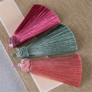 Può includere: Tre nappine di seta rosa, verde e rosa scuro. Ogni nappina ha una cima annodata e una piccola perla.