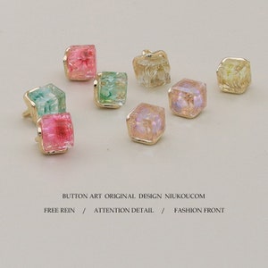 Puede incluir: Surtido de ocho botones pequeños, cuadrados, de resina con marcos de metal dorado. Los botones presentan varios colores y patrones, incluyendo rosa, verde y transparente.