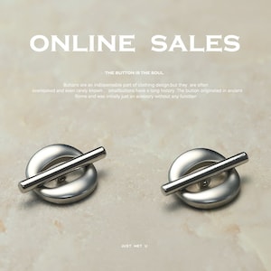 Könnte beinhalten: Zwei silberfarbene Metallknöpfe mit einem Balken in der Mitte. Die Knöpfe sind rund mit einem leicht erhöhten Rand. Der Text "ONLINE SALES" und "THE BUTTON IS THE SOUL" ist über den Knöpfen sichtbar. Der Text "JUST MET U" ist unter den Knöpfen sichtbar.