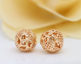 May include: Two gold-colored metal beads with intricate, openwork designs. The beads are round and have a delicate, filigree pattern.