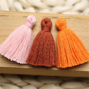 May include: Three colorful tassels in pink, brown, and orange. The tassels are made of yarn and are tied together at the top.
