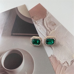 May include: A pair of gold-tone earrings with emerald green rectangular stones surrounded by clear rhinestones.
