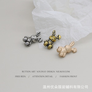 Puede incluir: Tres abalorios de metal en forma de conejo, en plata, oro y oro rosa. Los abalorios tienen forma de conejo de dibujos animados con un cuerpo cosido y orejas largas.  BUTTON ART YOUDUO DESIGN NIUKOUCOM FREE REIN / ATTENTION DETAIL / FASHION FRONT 温州优朵服装辅料有限公司