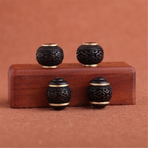 May include: Four black wooden beads with gold trim and a cloud design. The beads are arranged on a wooden surface.