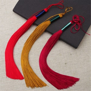 May include: Three long tassels with red, gold, and burgundy colored threads. The tassels are tied with a knot at the top and have a small decorative bead at the end.
