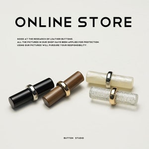 May include: Four decorative buttons in black, brown, pearlescent white, and glittery clear. Each button has a cylindrical shape with a metal ring. The text "ONLINE STORE" and "BUTTON STUDIO" are visible.
