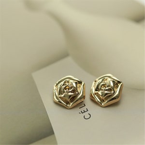 May include: A pair of gold-tone rose-shaped earrings. The earrings are made of metal and have a textured surface.