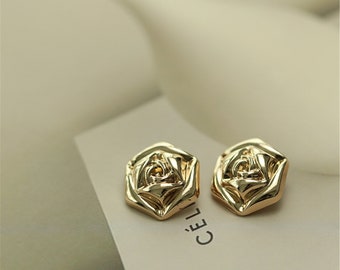May include: A pair of gold-tone rose-shaped earrings. The earrings are made of metal and have a textured surface.