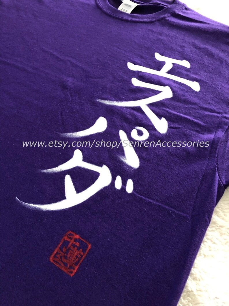 May include: A purple t-shirt with white Japanese characters and a red stamp. The text is stylized and appears to be hand-painted. The Etsy shop URL is visible at the bottom of the image.