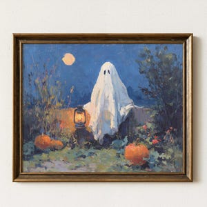 Könnte beinhalten: Gerahmtes Gemälde zeigt eine weiße Geisterfigur mit schwarzen Augen, beleuchtet von einer Laterne, unter einem Vollmond. Orangefarbene Kürbisse und Laubwerk befinden sich im Vordergrund, vor einem dunkelblauen Nachthimmel. Halloween-Thema.