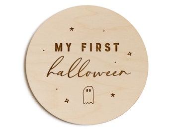 May include: A round wooden sign with the text "MY FIRST HALLOWEEN" and a small ghost illustration. The sign is decorated with small stars.