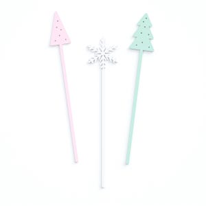 May include: Three decorative sticks with a pink Christmas tree, a white snowflake, and a green Christmas tree on top.