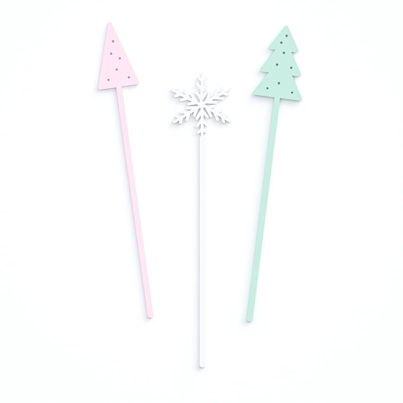 May include: Three decorative sticks with a pink Christmas tree, a white snowflake, and a green Christmas tree on top.
