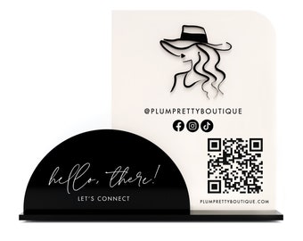 May include: Black and white business card holder with a white background and black text. The text says "hello, there!" and "Let's Connect". The business card holder has a QR code and social media icons. The business card holder is for the company "@plumprettyboutique".