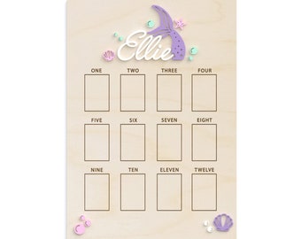 May include: A wooden board with a mermaid tail cutout and the name "Ellie" written in white. The board has 12 blank squares labeled with numbers one through twelve.