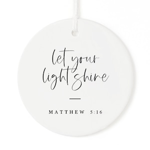 May include: White ceramic ornament with black calligraphy that reads "Let your light shine" and "Matthew 5:16".