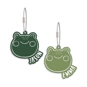 May include: Two green frog-shaped luggage tags with metal rings. The tag on the left says "JASON" and the tag on the right says "EMMA".