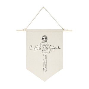 May include: A white canvas banner with a black line drawing of a girl wearing glasses and a skirt. The text "The future is female." is written in black cursive.