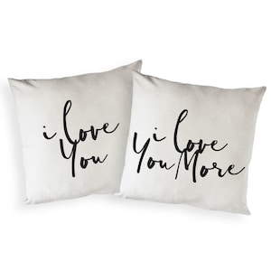 May include: Two white throw pillows with black text. One pillow says "I love you" and the other says "I love you more".