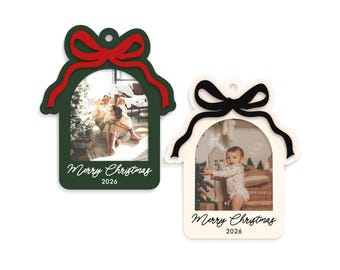 May include: Two custom photo ornaments shaped like houses with arched windows. One is dark green with a red bow and the other is cream with a black bow. Both feature a printed photograph, the text Merry Christmas, and the year 2026 at the bottom.