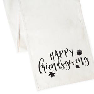 May include: White table runner with black text that reads "Happy Friendsgiving" with a small acorn and leaf graphic.