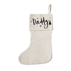 May include: A white Christmas stocking with a black "Daddy" design and a small tree graphic. The stocking has a white cuff with black snowflakes.