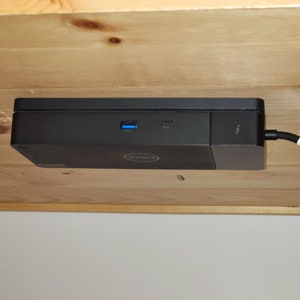 May include: A black Dell computer is mounted under a wooden desk. The computer has a power cord plugged in and two ports on the side. The ports are labeled "USB" and "HDMI".