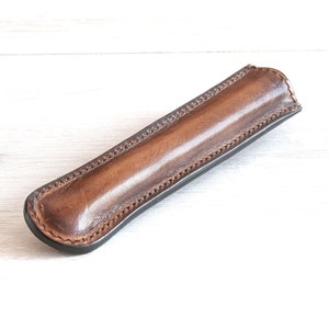 May include: A brown leather pen case with a stitched edge.