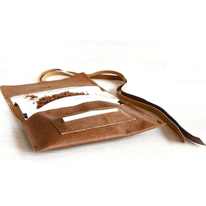 Peut inclure: Une pochette à tabac en cuir marron avec un rabat et une sangle. La pochette est ouverte et il y a du tabac à l'intérieur.