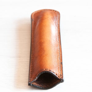 May include: A brown leather pen case with a stitched seam. The case is open and ready to hold a pen.