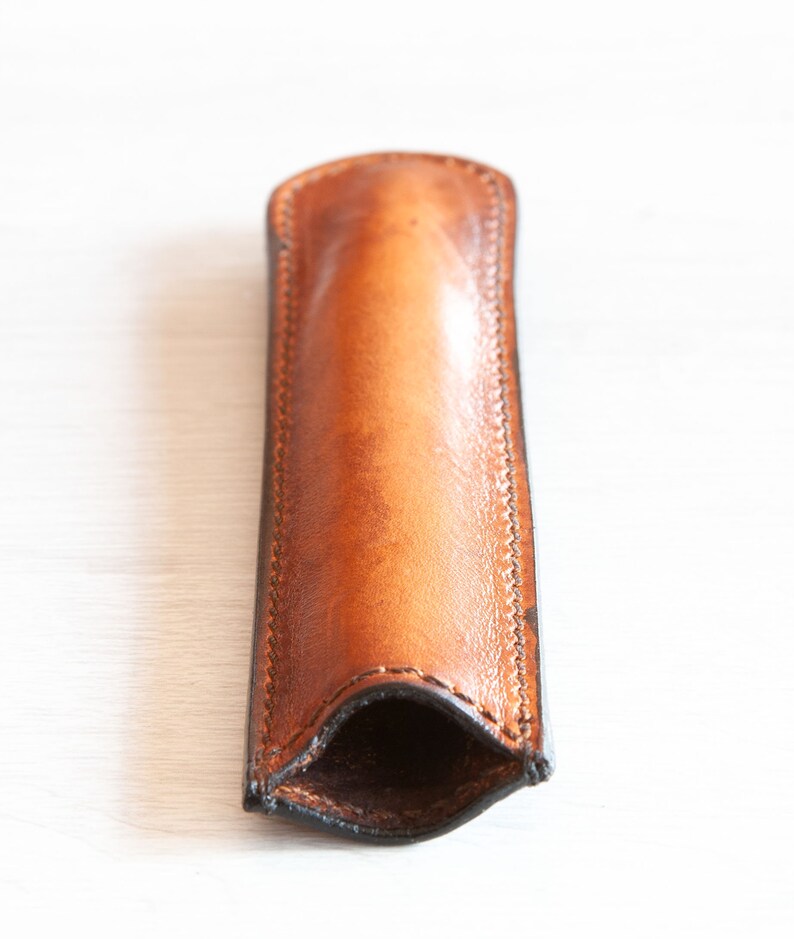 May include: A brown leather pen case with a stitched seam. The case is open and ready to hold a pen.