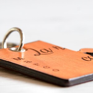 May include: A wooden keyring with a rectangular tag and a small circular accent. The tag is light brown with dark brown edges and features engraved text. A silver metal ring is attached for keys.