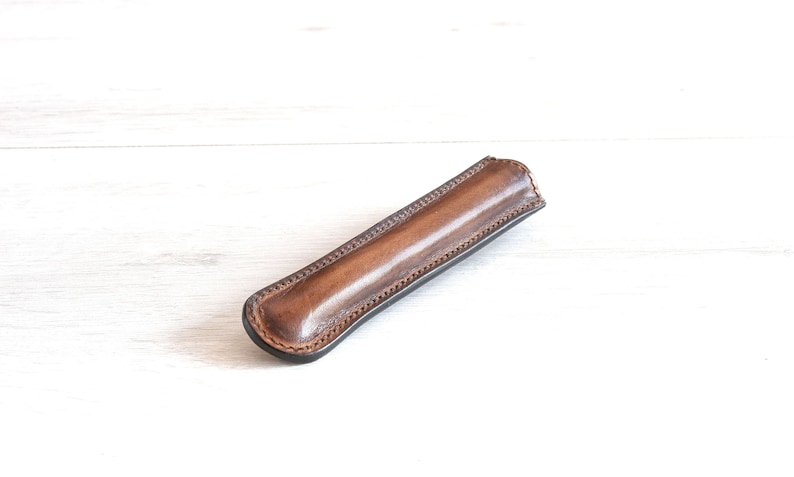 May include: A brown leather pen case with a stitched edge.