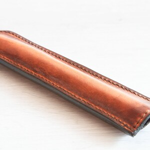 May include: A brown leather pen case with a stitched edge.